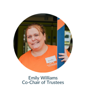 Emily, holding a blue and orange frame, looking at the camera smiling. Emily wears an orange Active Impact photo